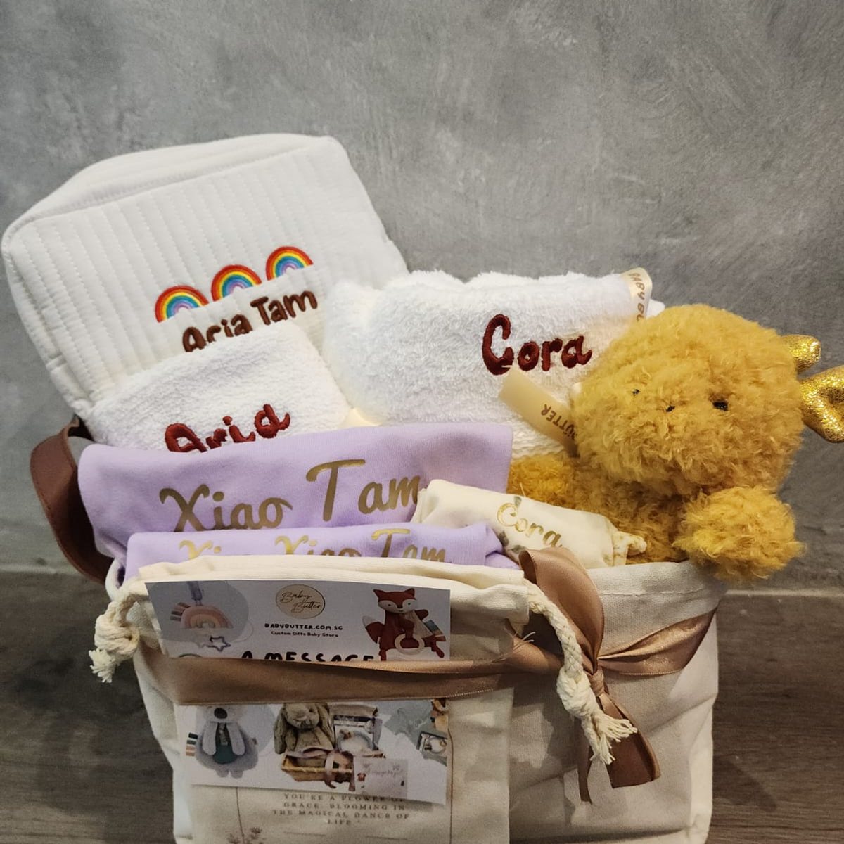 A Baby Butter gift basket with towels, a pouch and rompers embroidered with names
